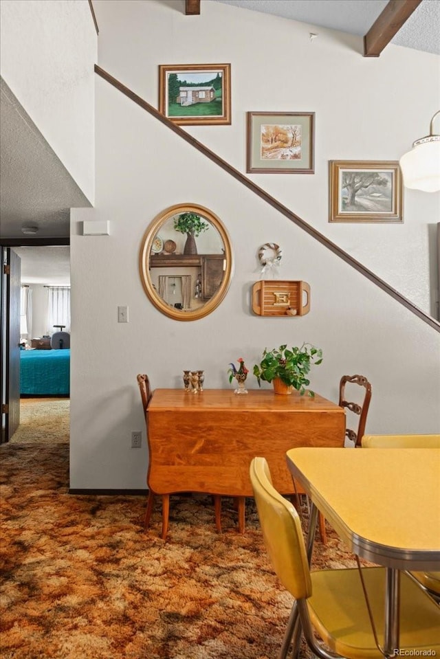 dining area featuring a textured ceiling, carpet flooring, and vaulted ceiling with beams