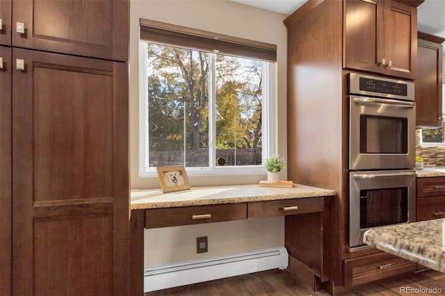 kitchen with light stone counters, stainless steel double oven, dark wood-type flooring, and a baseboard heating unit