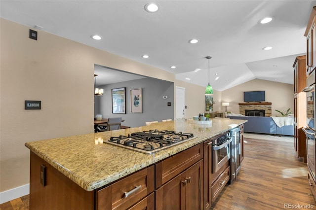 kitchen with stainless steel gas cooktop, wood-type flooring, a fireplace, a center island, and lofted ceiling