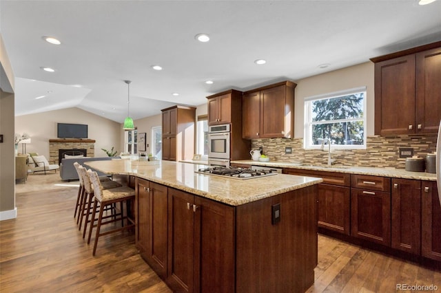 kitchen featuring hardwood / wood-style floors, a center island, a stone fireplace, vaulted ceiling, and appliances with stainless steel finishes