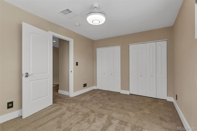 unfurnished bedroom featuring light colored carpet and multiple closets