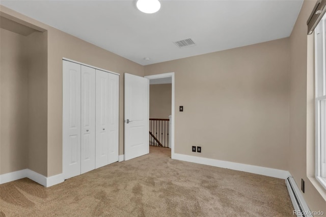 unfurnished bedroom with baseboard heating, a closet, and carpet