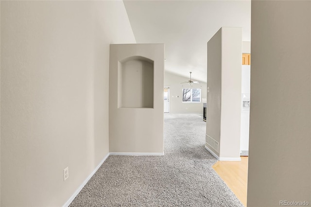 hall featuring light carpet, baseboards, and vaulted ceiling