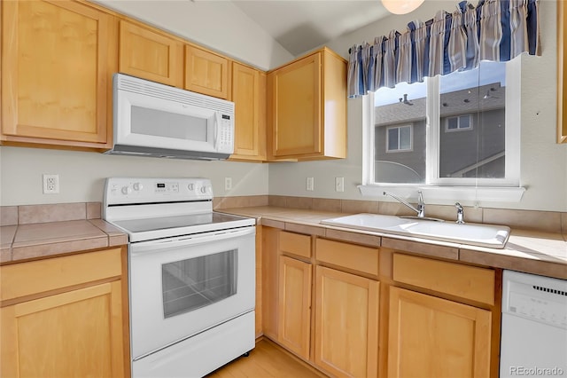 kitchen with light brown cabinetry, light countertops, light wood-style floors, white appliances, and a sink