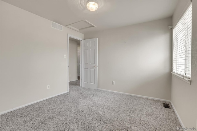 carpeted spare room with visible vents, baseboards, and attic access