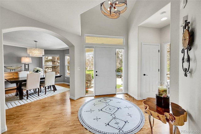 entryway with visible vents, arched walkways, baseboards, a chandelier, and light wood-style floors