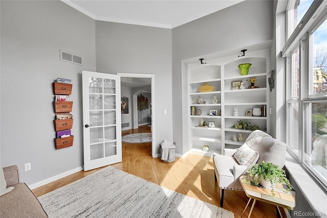 living area featuring visible vents, wood finished floors, baseboards, ornamental molding, and a high ceiling
