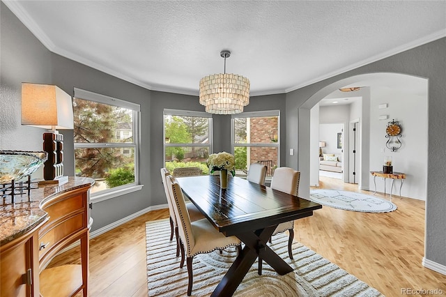 dining room with a notable chandelier, light wood-style floors, arched walkways, a textured ceiling, and ornamental molding
