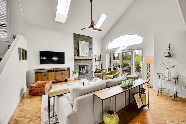 living room featuring a fireplace, baseboards, high vaulted ceiling, light wood-style flooring, and a skylight