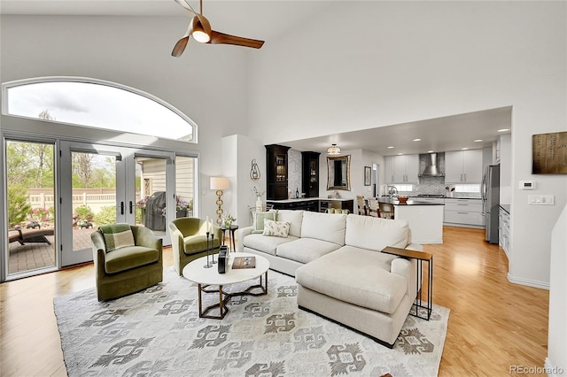 living area featuring a ceiling fan, a high ceiling, french doors, and light wood-type flooring