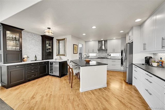 kitchen with freestanding refrigerator, wine cooler, wall chimney range hood, light wood finished floors, and backsplash