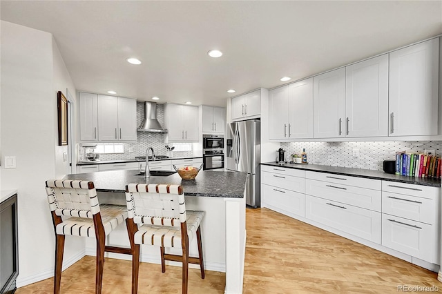 kitchen featuring decorative backsplash, a kitchen breakfast bar, white cabinets, stainless steel appliances, and wall chimney exhaust hood