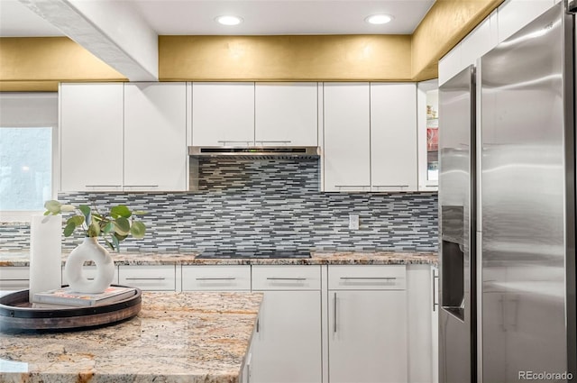 kitchen with stainless steel fridge with ice dispenser, light stone countertops, black electric cooktop, white cabinets, and tasteful backsplash