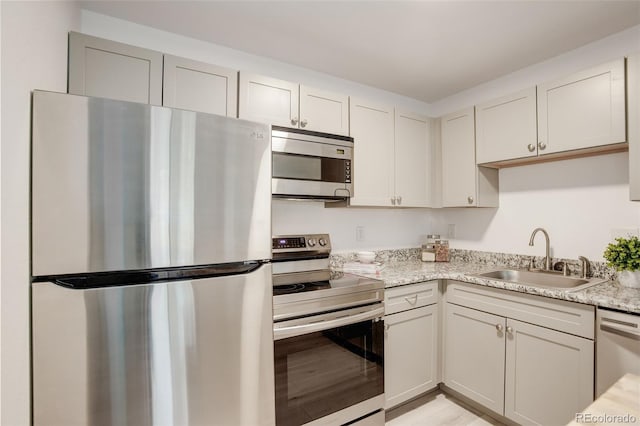 kitchen featuring stainless steel appliances, light stone countertops, and a sink