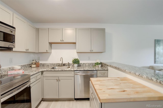 kitchen featuring a sink, light wood-style flooring, wooden counters, and appliances with stainless steel finishes