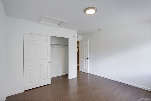 unfurnished bedroom with attic access, dark wood finished floors, a closet, and baseboards