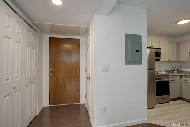 hallway featuring electric panel, baseboards, and light wood-style floors
