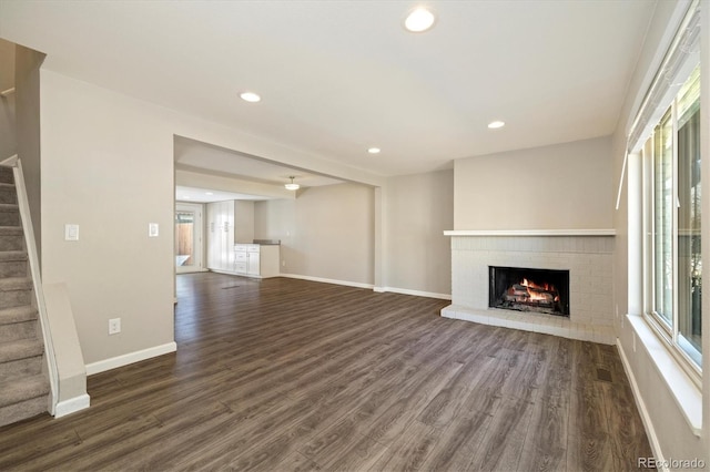 unfurnished living room featuring stairway, a brick fireplace, dark wood-type flooring, and a healthy amount of sunlight