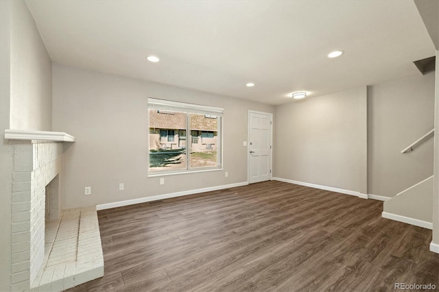 unfurnished living room featuring a brick fireplace, baseboards, dark wood finished floors, stairs, and recessed lighting