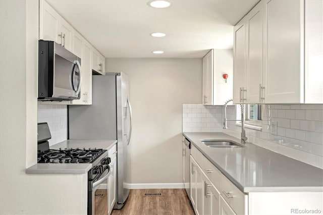 kitchen with a sink, stainless steel appliances, white cabinets, and light wood finished floors