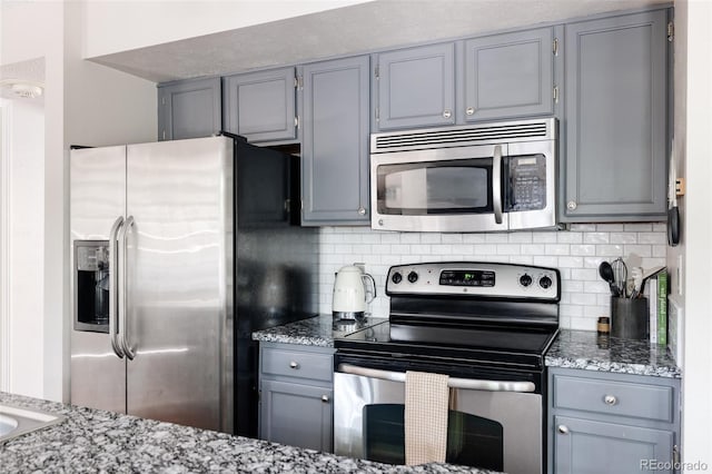 kitchen with gray cabinetry, light stone countertops, tasteful backsplash, and stainless steel appliances