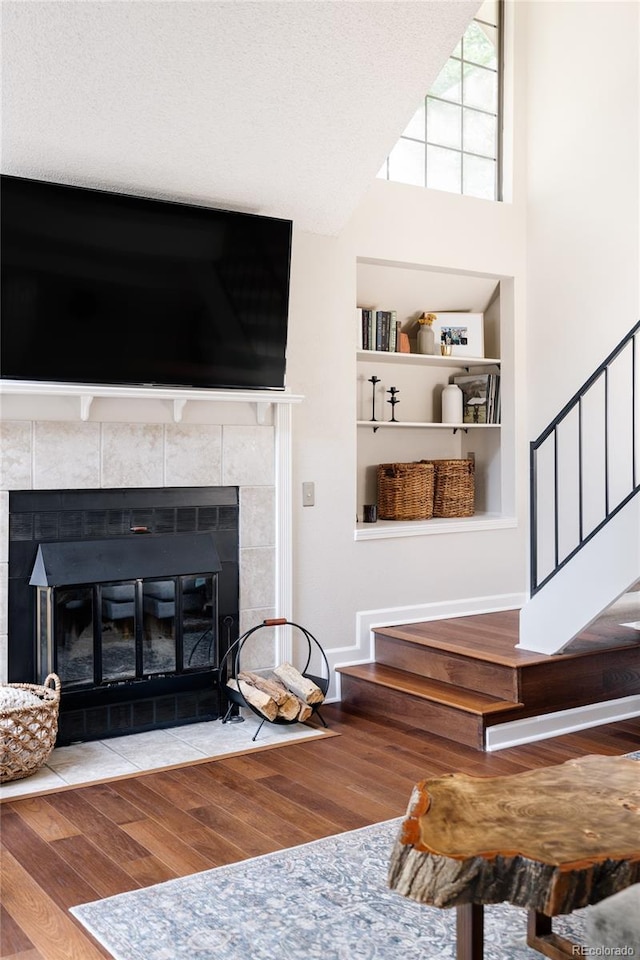 unfurnished living room with hardwood / wood-style flooring, a tile fireplace, built in shelves, and a textured ceiling