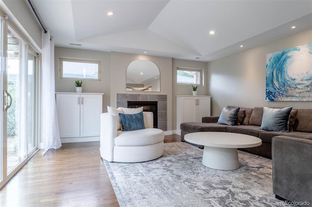 living room with lofted ceiling, a tiled fireplace, light wood-type flooring, and a wealth of natural light