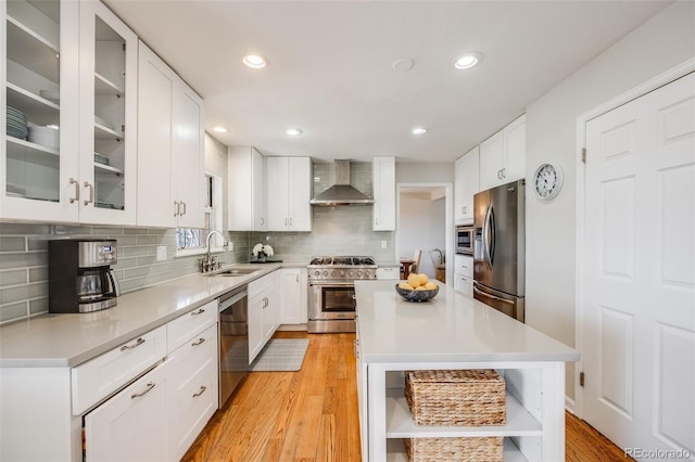 kitchen with wall chimney range hood, sink, white cabinets, and appliances with stainless steel finishes