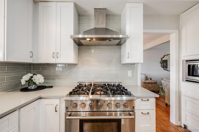 kitchen featuring wall chimney range hood, backsplash, white cabinets, and appliances with stainless steel finishes