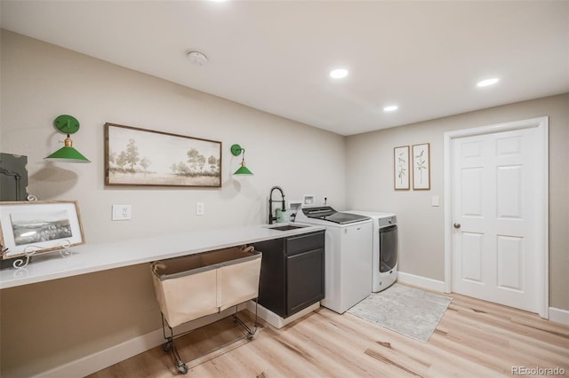 clothes washing area with cabinets, sink, washing machine and clothes dryer, and light wood-type flooring