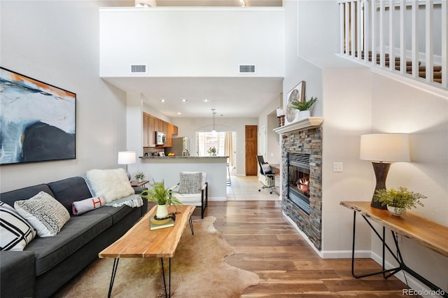 living room with light wood-type flooring, a fireplace, a towering ceiling, and visible vents