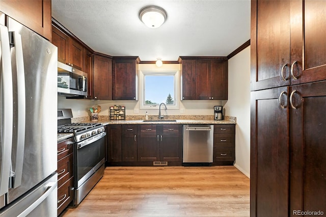 7830 Club Crest Dr, Arvada, CO 80005 - kitchen featuring appliances with stainless steel finishes, light wood-type flooring, dark brown cabinets, light stone counters, and crown molding