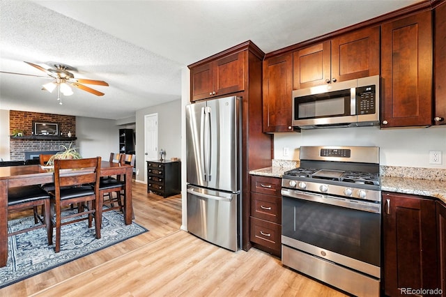 7830 Club Crest Dr, Arvada, CO 80005 - kitchen with appliances with stainless steel finishes, light wood-style floors, a ceiling fan, light stone counters, and a brick fireplace