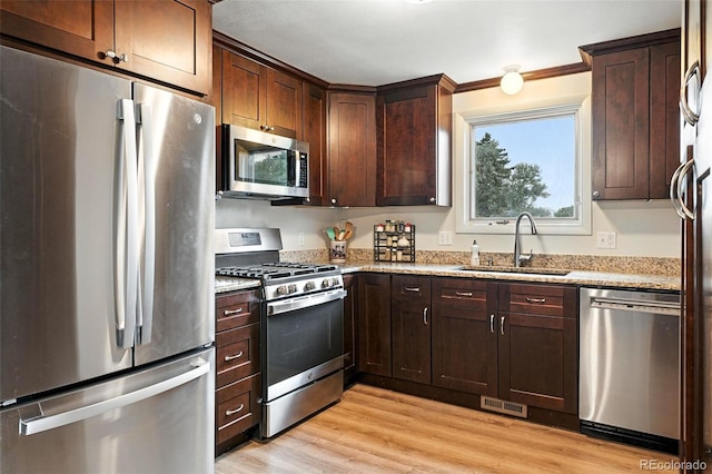 7830 Club Crest Dr, Arvada, CO 80005 - kitchen with stainless steel appliances, light stone countertops, light wood-style floors, dark brown cabinetry, and ornamental molding