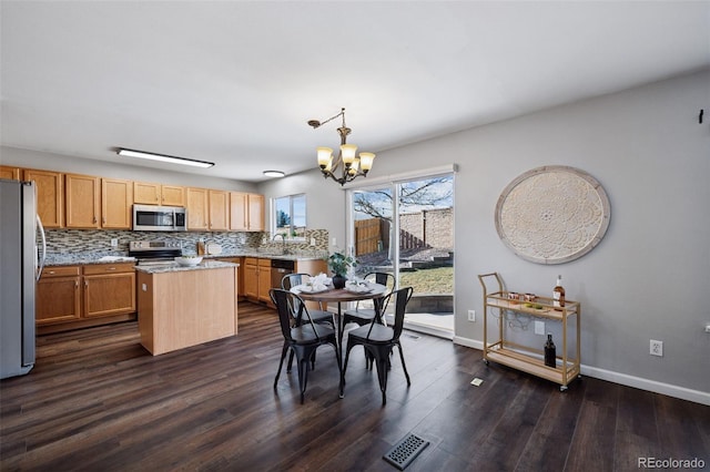 kitchen with a sink, a kitchen island, appliances with stainless steel finishes, decorative backsplash, and an inviting chandelier