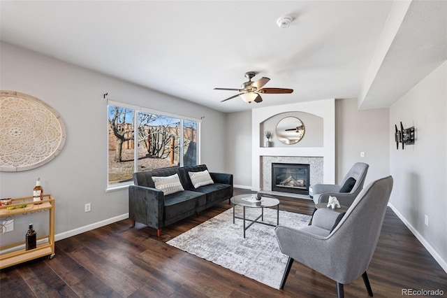 living area with a ceiling fan, a premium fireplace, baseboards, and wood finished floors