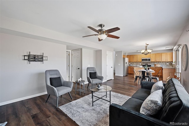 living area with dark wood-style floors, baseboards, and ceiling fan with notable chandelier