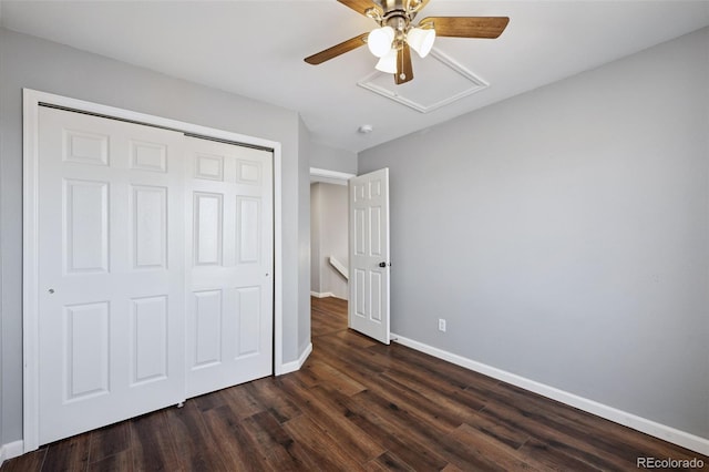 unfurnished bedroom with attic access, baseboards, a ceiling fan, dark wood-type flooring, and a closet