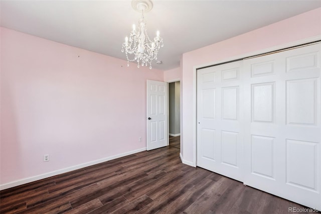 unfurnished bedroom featuring dark wood-type flooring, a closet, an inviting chandelier, and baseboards