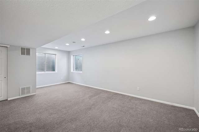 empty room with carpet floors, baseboards, visible vents, and a textured ceiling