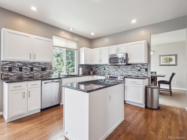 kitchen featuring dark countertops, stainless steel appliances, wood finished floors, and white cabinetry