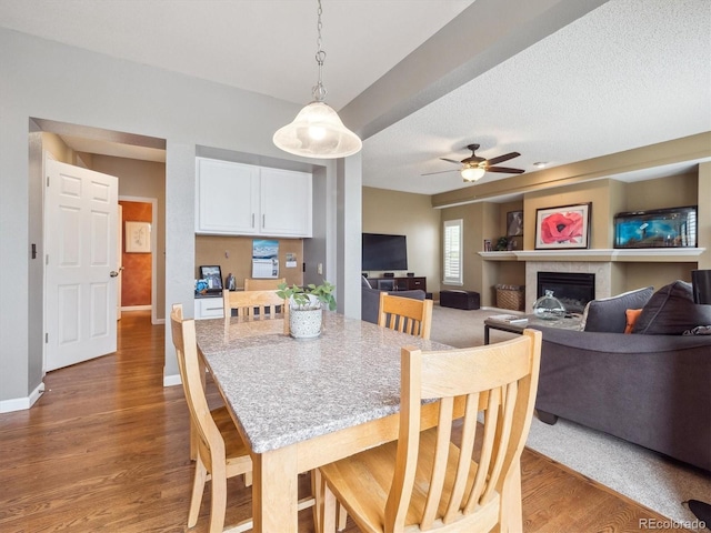 dining room with a glass covered fireplace, baseboards, a ceiling fan, and wood finished floors