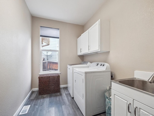 washroom with cabinet space, washer and dryer, a sink, wood finished floors, and visible vents