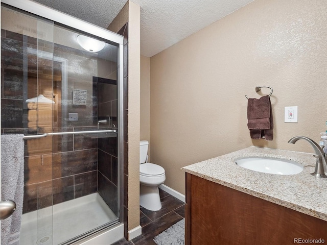 bathroom with vanity, a textured wall, toilet, a textured ceiling, and a shower stall