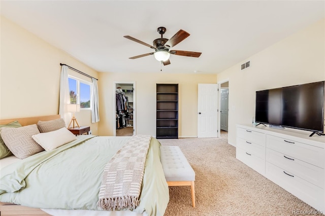 carpeted bedroom with a walk in closet and ceiling fan