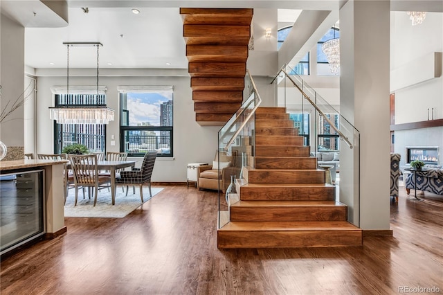 staircase featuring a tile fireplace, a towering ceiling, wine cooler, and a chandelier