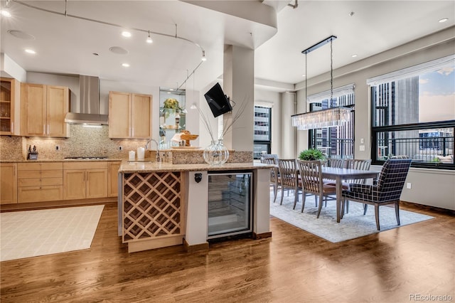 kitchen featuring wine cooler, gas cooktop, light brown cabinets, and wall chimney range hood