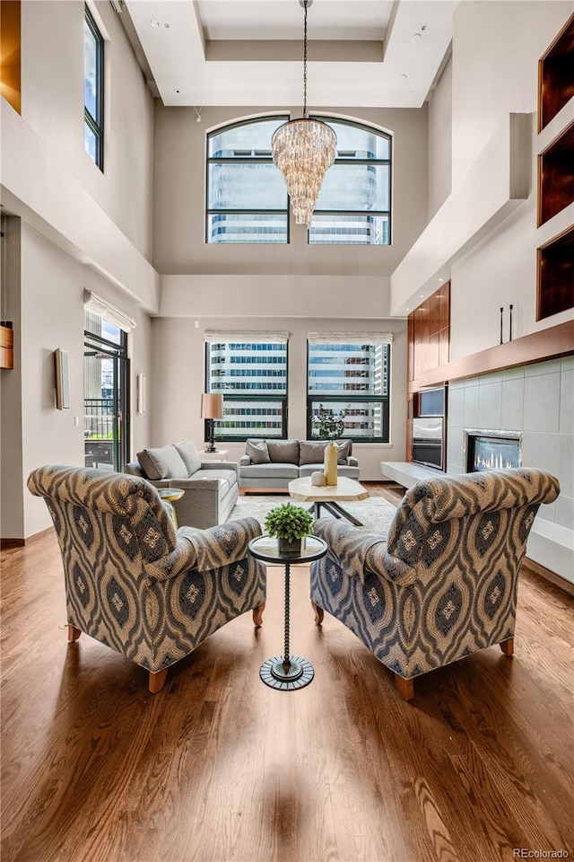 living room with a tiled fireplace, light hardwood / wood-style flooring, a raised ceiling, and a chandelier