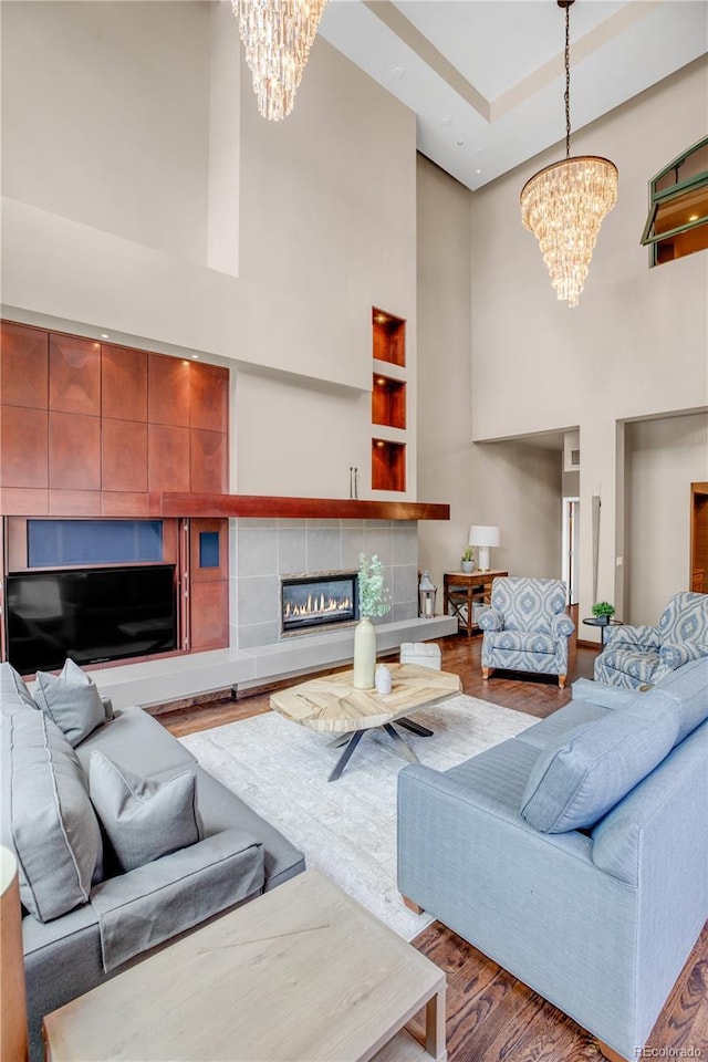 living room featuring hardwood / wood-style flooring, built in features, a towering ceiling, a notable chandelier, and a fireplace