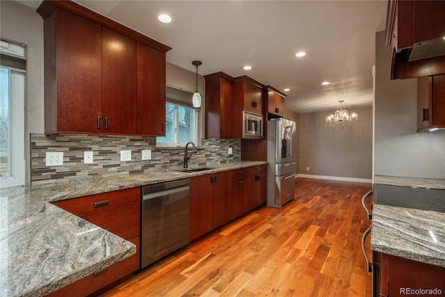 kitchen with light wood-style flooring, a sink, hanging light fixtures, appliances with stainless steel finishes, and backsplash